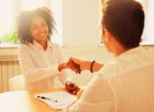 Smiling millennial african woman handshaking partner at office meeting, happy black female manager and satisfied male client or colleague shaking hands making deal or thanking for help in teamwork