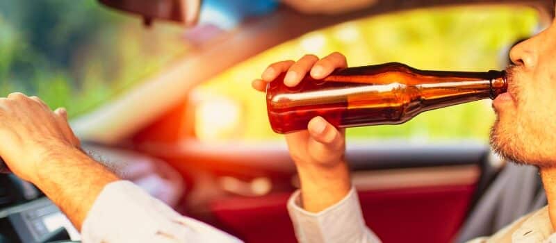 Drunk asian young man drives a car with a bottle of beer with sunset background, Dangerous driving concept