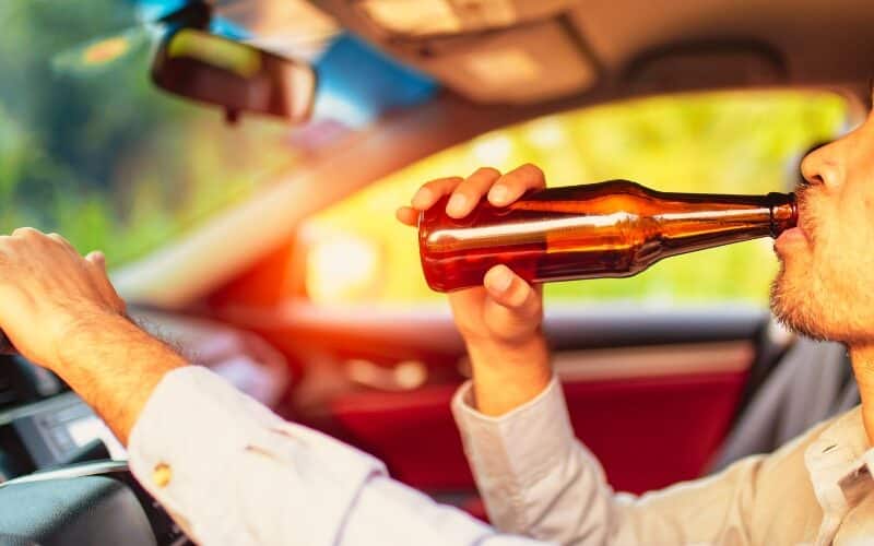 Drunk asian young man drives a car with a bottle of beer with sunset background, Dangerous driving concept