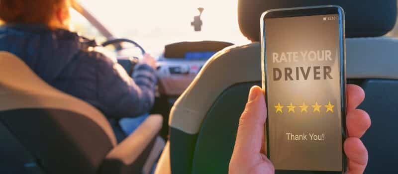 Passenger is sitting on the back seat of the car and using smart phone app to rate a driver. Taxi or modern peer to peer ridesharing concept