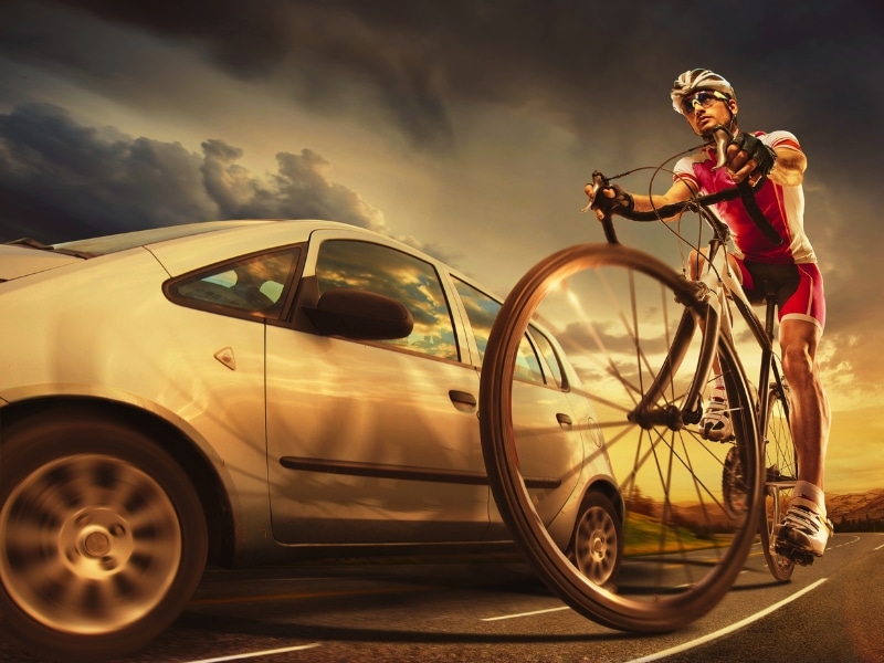Speeding car passing beside cyclist on the road