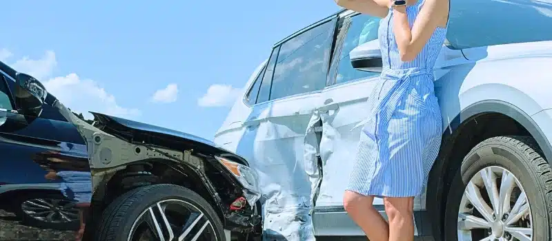 A frustrated woman using her mobile phone after a car crash.