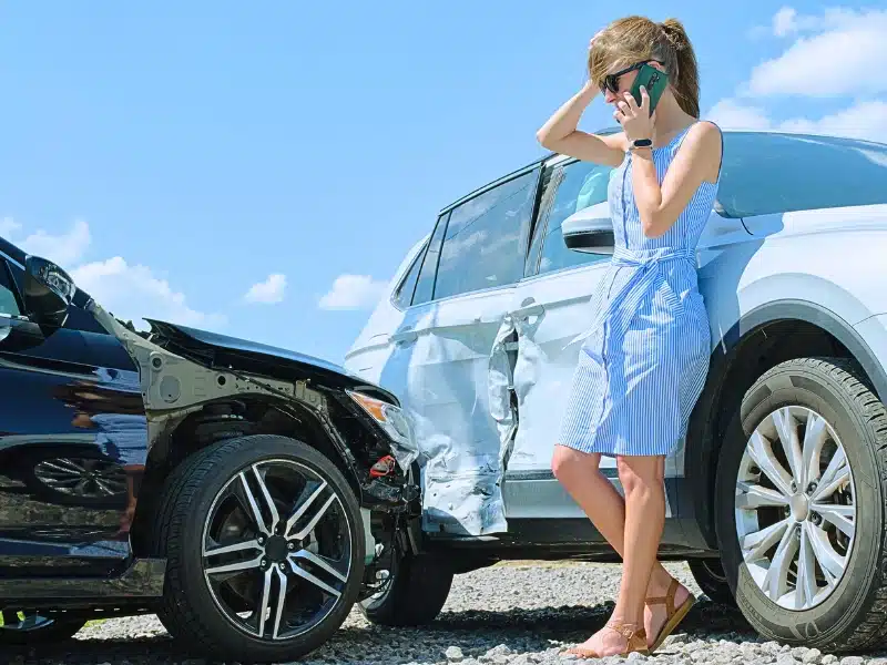 A frustrated woman using her mobile phone after a car crash.