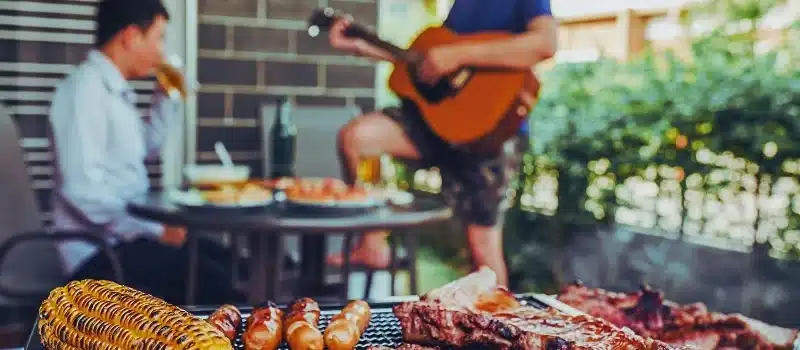 Griller and BBQ with two guys drinking alcohol in the background.