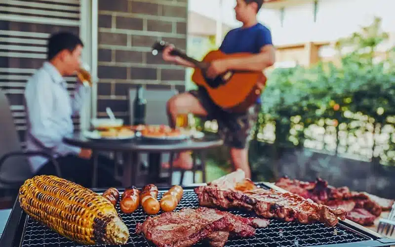 Griller and BBQ with two guys drinking alcohol in the background.
