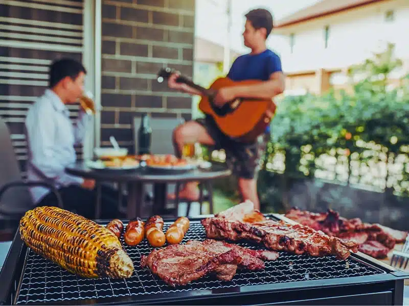 Griller and BBQ with two guys drinking alcohol in the background.