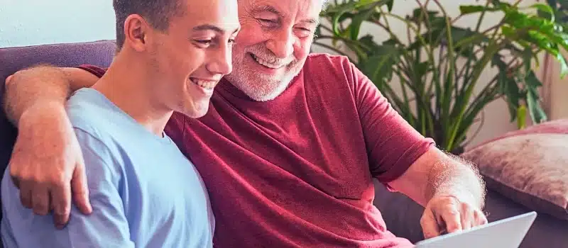 Father and son sitting on the couch looking at the laptop and both smiling.