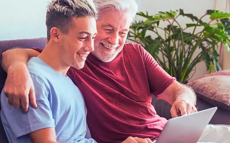 Father and son sitting on the couch looking at the laptop and both smiling.