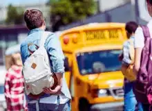 Rear view of group of teen students with backpacks walking to school bus after school. Sue for a school bus accident