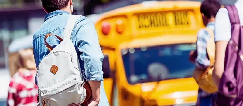 Rear view of group of teen students with backpacks walking to school bus after school. Sue for a school bus accident