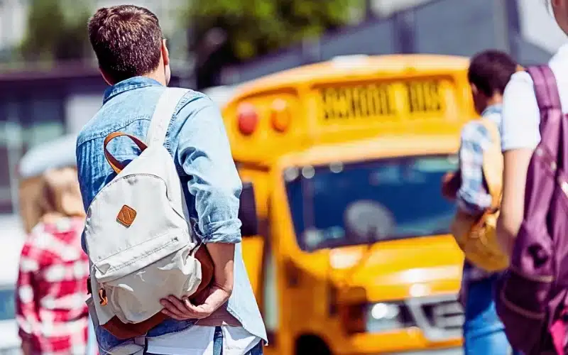 Rear view of group of teen students with backpacks walking to school bus after school. Sue for a school bus accident