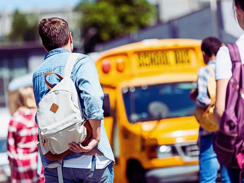 Rear view of group of teen students with backpacks walking to school bus after school. Sue for a school bus accident
