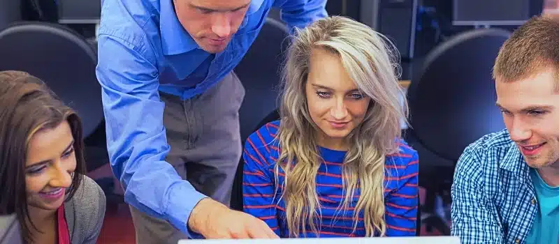 Teacher showing something on screen to students in computer room.