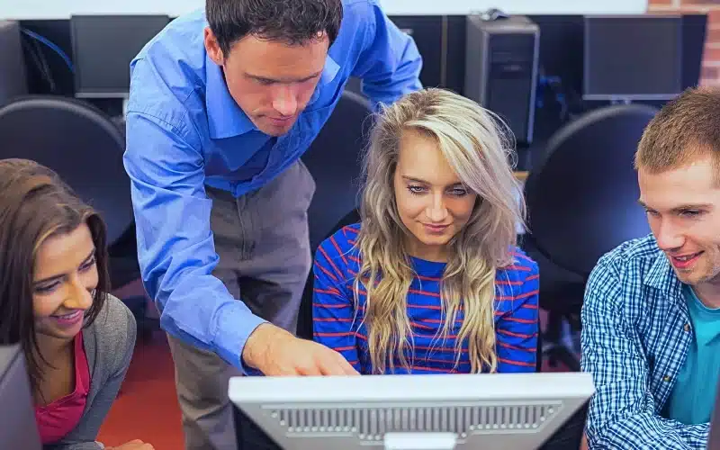 Teacher showing something on screen to students in computer room.
