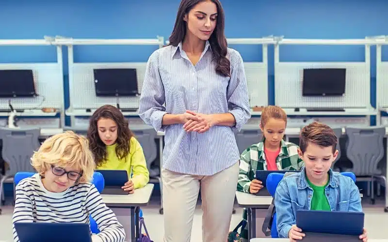 Woman standing watching students working on tablets.