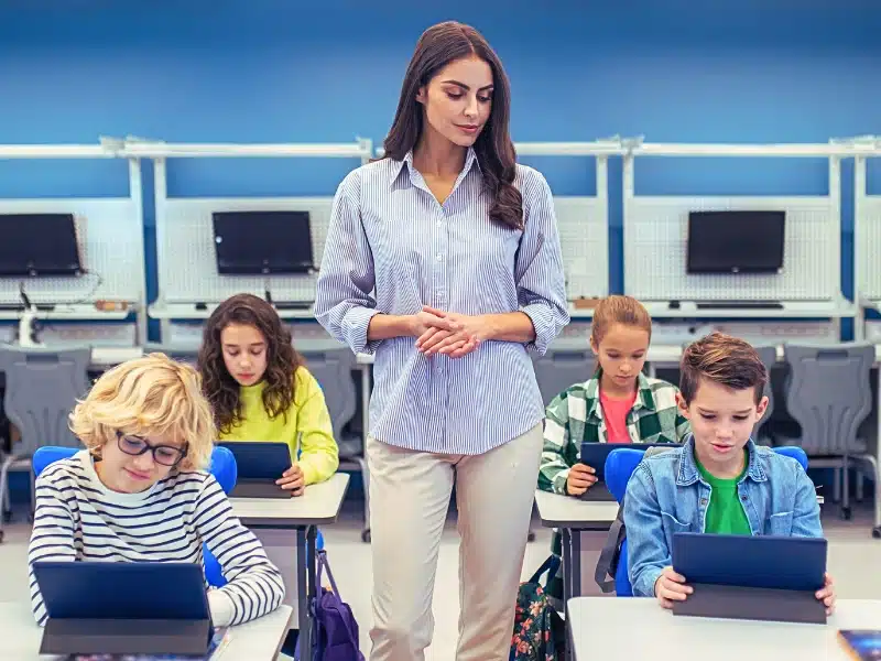 Woman standing watching students working on tablets.
