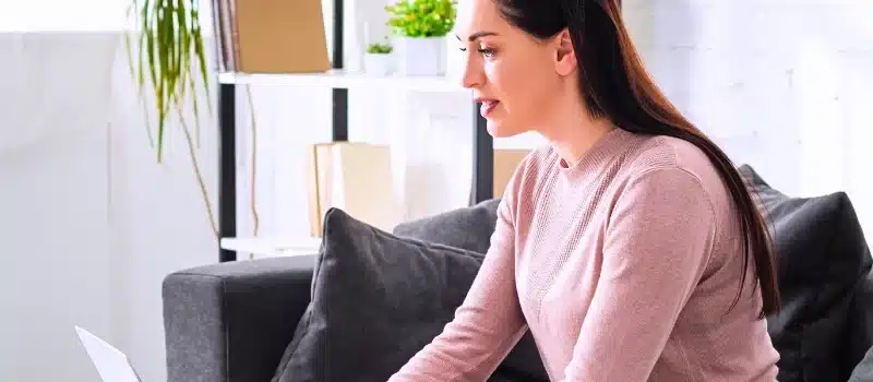 Woman working on a laptop in a comfortable, home-like setting.