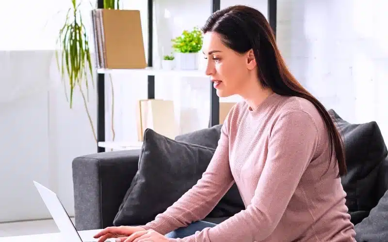 Woman working on a laptop in a comfortable, home-like setting.