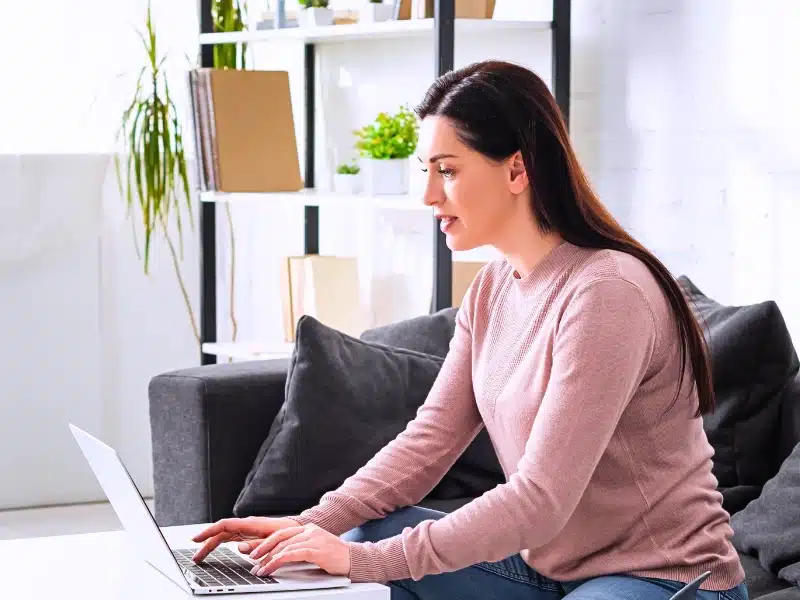 Woman working on a laptop in a comfortable, home-like setting.